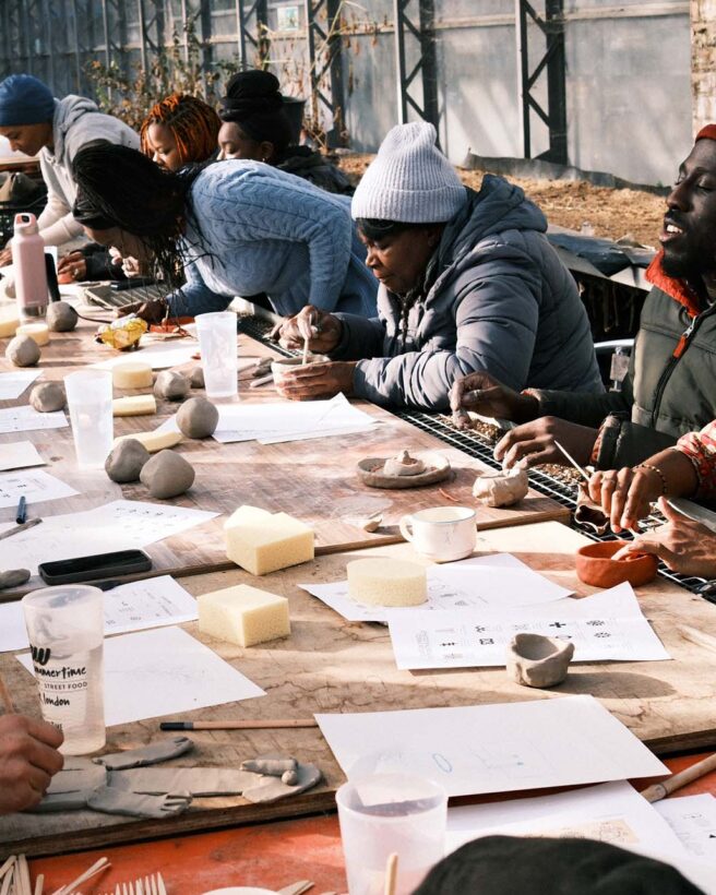 The image shows a group of people taking part in an arts and crafts workshop. There is a long table with paper and other crafts materials.