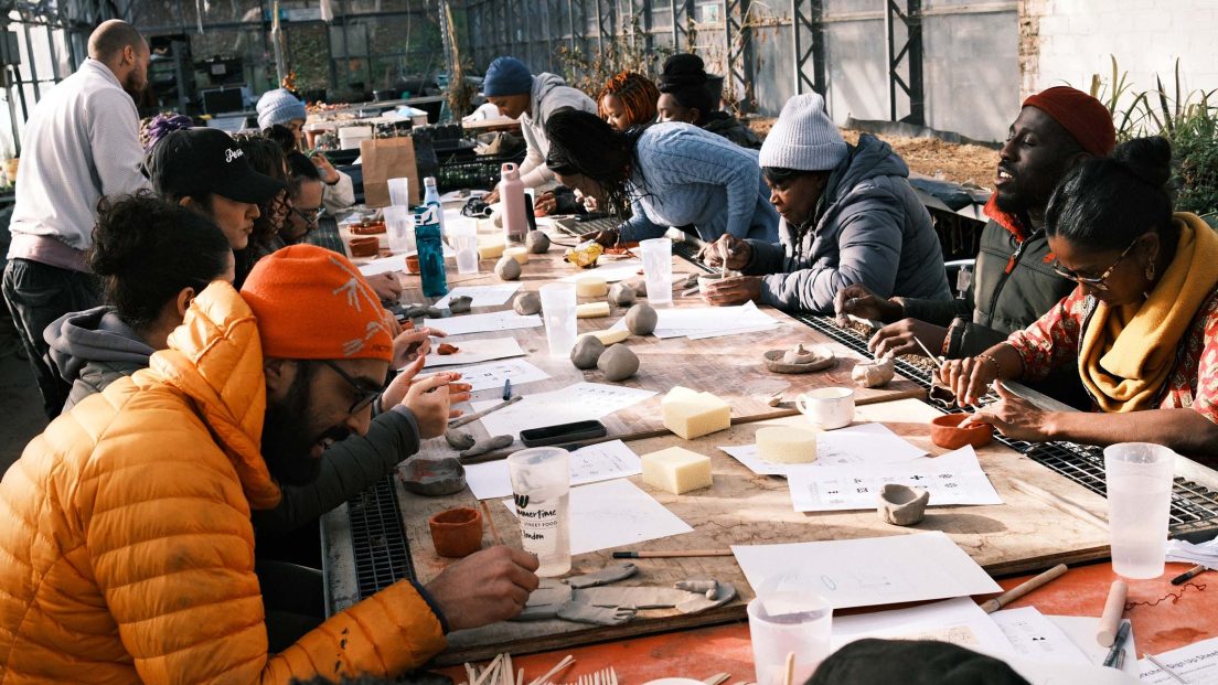 The image shows a group of people taking part in an arts and crafts workshop. There is a long table with paper and other crafts materials.
