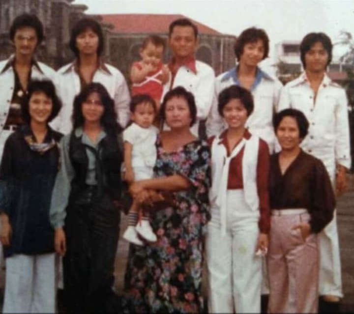 The image shows a picture of Mitzi's family from the 70s, standing in the plaza looking at the camera. 