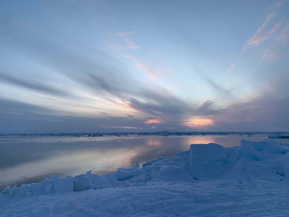 The image is of an Arctic landscape with ice sheets and a vast sky with clouds