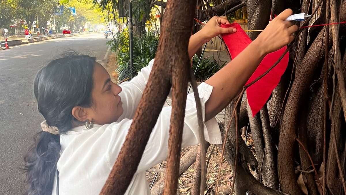 the image shows a woman in a white top tying a read heart to a tree