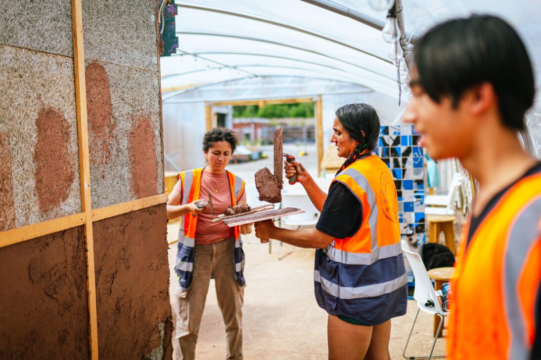 the image shows two people in orange high res jackets plastering a wall together