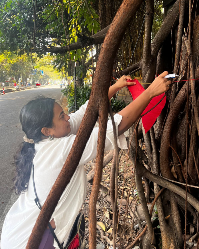 the image shows a woman in a white top tying a read heart to a tree