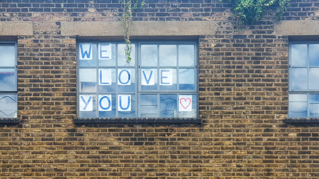 the image shows a building with three windows. In the middle window we can see the words we love you stuck on to the window