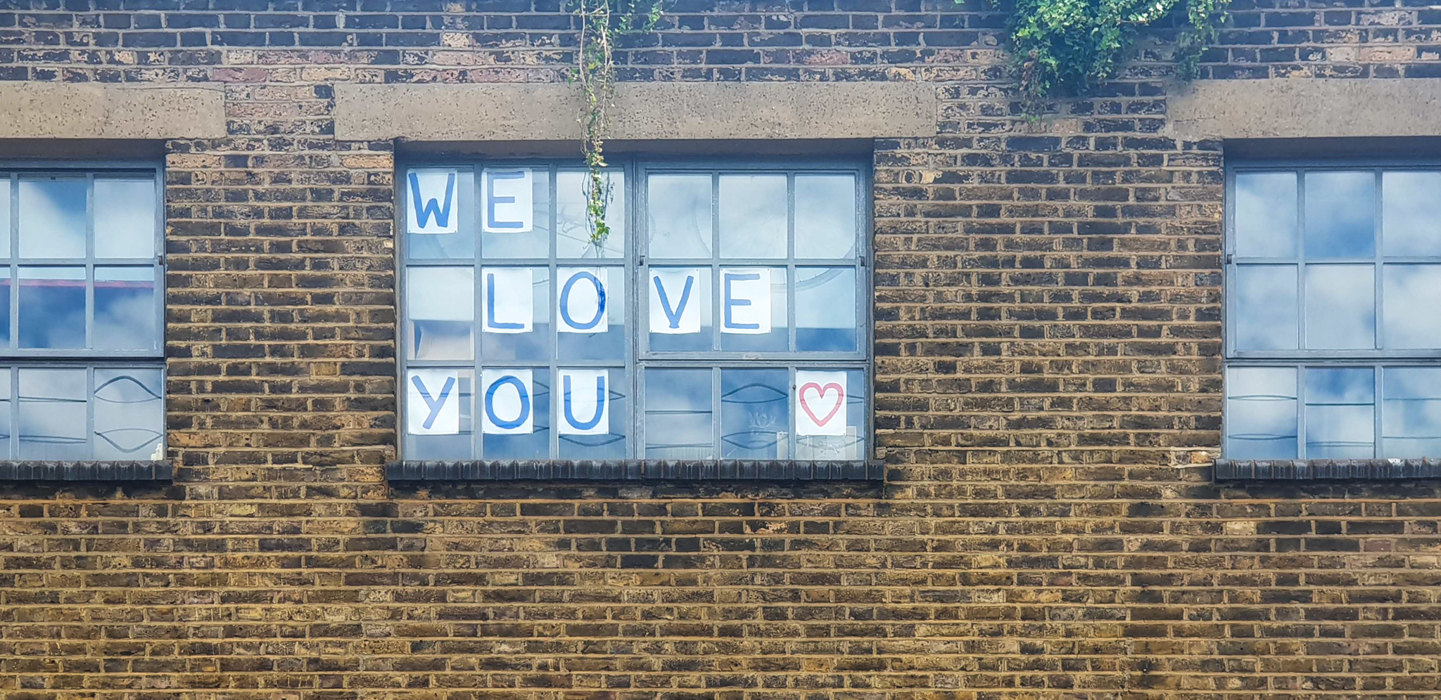 the image shows a building with three windows. In the middle window we can see the words we love you stuck on to the window
