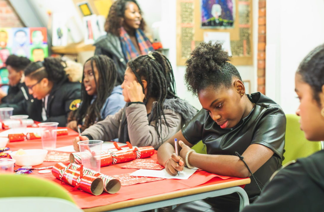 the image shows a group of young people sat at a table taking part in a writing exercise.