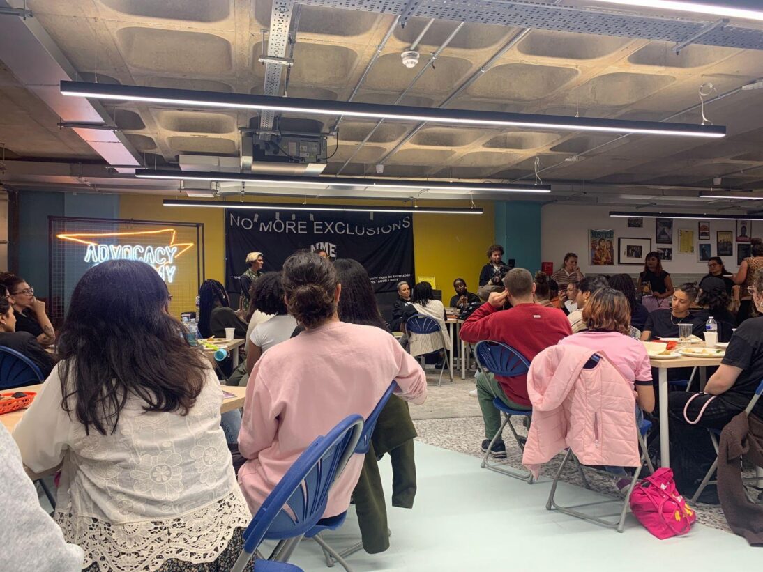 there is a group of young people sat at tables listening to a presentation. they have their backs to the viewer