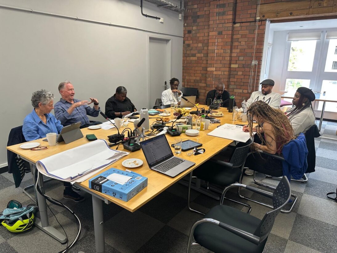 Photo of Reframing the Frame roundtable facilitated by Professor Shawn Sobers. the image shows a group of people of all ages sat around a table discussing.