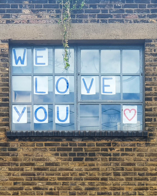 the image shows a building with three windows. In the middle window we can see the words we love you stuck on to the window