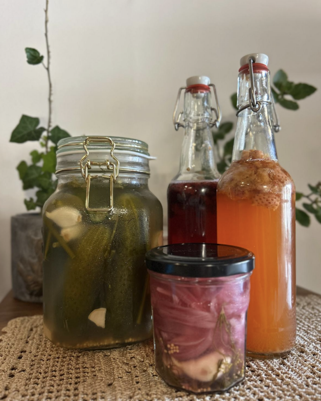 the image shows a row of jars of pickled gherkins on a marble working top